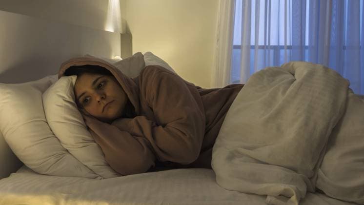 Erschöpfte junge Frau, die zusammengerollt im dunklen Schlafzimmer auf dem Bett liegt, einen Hoodie trägt und ausdruckslos starrt. Sie drückt Depressionen, emotionales Burnout und Hilflosigkeit, psychische Krise und Schlafstörungen aus Exhausted young woman lying curled on bed in dim bedroom, wearing hoodie and staring blankly, expressing depression, emotional burnout and helplessness, mental health crisis and insomnia concept Copyright: imageBROKER EvgeniiaxGordeeva ibxiqx18667283.jpg ,model released, Symbolfoto ,property released