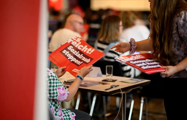 Delegates distribute posters reading Stop Social Plunder—Enough Is Enough on September 19, 2026, at the Die Linke NRW State Party Convention, held on September 19–20, 2026, at the Stadthalle in Mülheim an der Ruhr, Germany.