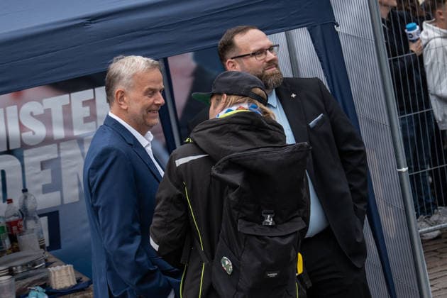 AfD candidate for minister-president Leif Eric Holm, wearing a blue suit, talks with streamer Sebastian Weber—known as Weichreite TV—who is carrying a backpack backstage during the event in Schwerin marking the conclusion of the AfD’s campaign for the 2026 state election in Mecklenburg-Western Pomerania, in Schwerin, Schwerin, Mecklenburg-Western Pomerania, Germany, Am Markt