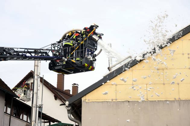 Two firefighters in the aerial ladder truck are spraying foam into the building; behind them is the basket of another aerial ladder truck. Fire in the former workshop building of Naturstein Stefan Wormser, Pestalozzistraße and Friedhofsweg, 20 09 2026, Upper Franconia, Bavaria,
