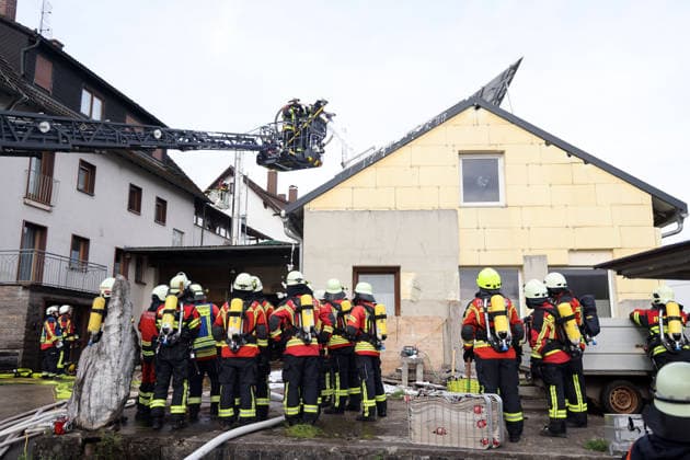 Two firefighters in the turntable ladder are spraying foam into the building while other emergency responders wait outside. Fire at the former Naturstein Stefan Wormser workshop building, Pestalozzistraße and Friedhofsweg, 20 09 2026, Upper Franconia, Bavaria,