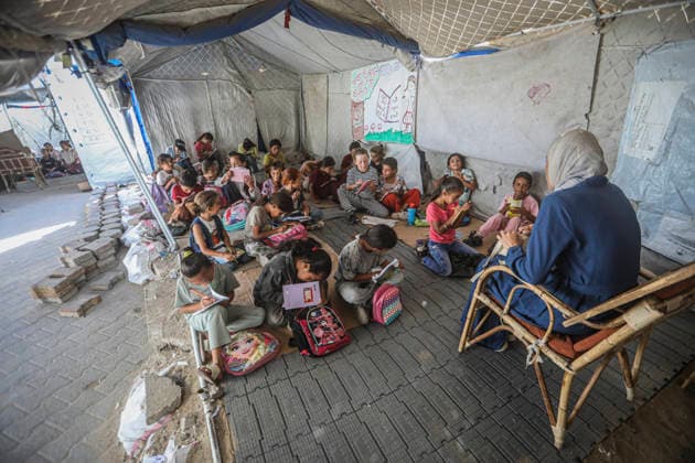 Gaza Temporary Tent Classrooms Palestinian children sit on the floor around a teacher inside a temporary classroom tent in western Gaza City, Gaza Strip on September 20, 2026. Thousands of Palestinian children in the Gaza Strip have resumed lessons in temporary classrooms as the education system continues to face widespread disruption and damage following the war. Temporary learning spaces, including tents, are being used as schools and educational facilities remain damaged or unavailable. Gaza Gaza Strip Palestinian Territories Copyright: xFaizxQreqax