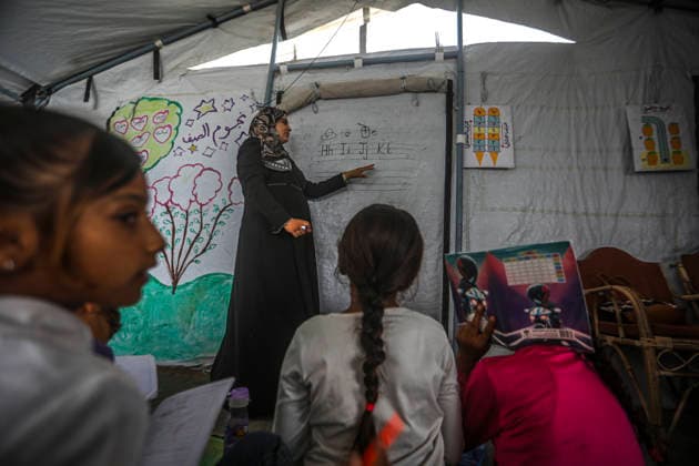 Gaza Temporary Tent Classrooms A teacher points to writing on a makeshift board during a lesson inside a temporary classroom tent in western Gaza City, Gaza Strip on September 20, 2026. Thousands of Palestinian children in the Gaza Strip have resumed lessons in temporary classrooms as the education system continues to face widespread disruption and damage following the war. Temporary learning spaces, including tents, are being used as schools and educational facilities remain damaged or unavailable. Gaza Gaza Strip Palestinian Territories Copyright: xFaizxQreqax