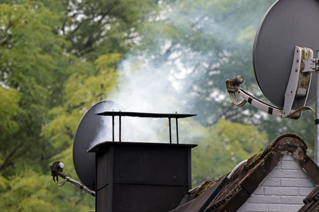Smoke from a chimney; a chimney emitting smoke from a clean-burning fire on a roof at the start of the heating season in the fall, when temperatures are low