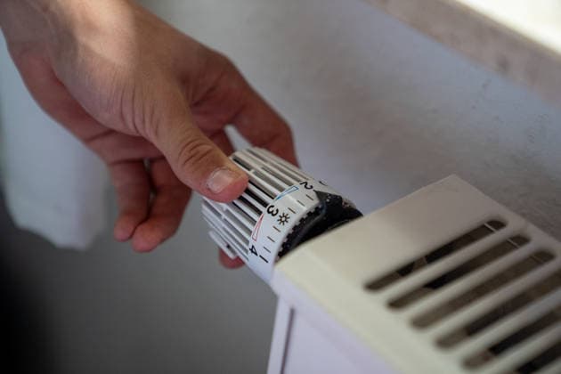 A hand turning the thermostat knob on a radiator. Stock image related to heating, heating costs, energy consumption, and energy conservation. Copyright: xSvenxHeidmannx
