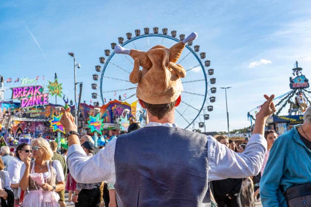 Oktoberfest 2026: A festivalgoer wearing a Hendl hat spreads good cheer at the Wiesn, forming finger hearts with his hands—a symbol o