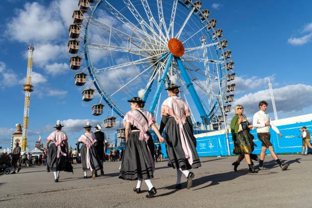 Oktoberfest 2026, female festivalgoers in traditional dress stroll across the festival grounds in bright sunshine, past the Ferris wheel, the most beautiful blue-and-white Oktoberfest weather, Munich, September 22, 2026, German