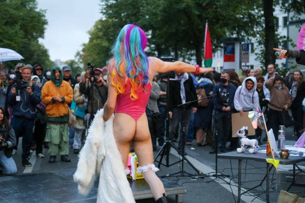 Berlin, Germany, September 24, 2026 Performance at the protest rally against the presentation of the Axel Springer Award to Peter Thiel A scantily clad person wearing a rainbow-colored wig appears in front of demonstrators, with a Palestinian flag in the background Demonstration, Protest, Performance, Peter Thiel, Palantir Copyright: xAlonxDavidx