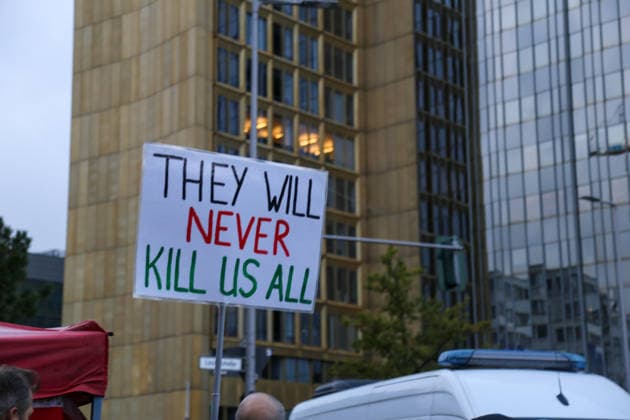 Berlin, Germany, September 24, 2026: A protest sign reading THEY WILL NEVER KILL US ALL in front of the Axel Springer skyscraper during a rally against the presentation of the Axel Springer Award to Peter Thiel. A police vehicle is visible in the foreground. Demonstration, protest, Peter Thiel, Palantir, Axel Sp Copyright: xAlonxDavidx