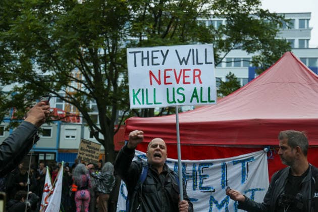 Berlin, Germany, September 24, 2026: A protester with a raised fist and a protest sign reading THEY WILL NEVER KILL US ALL at a rally against the presentation of the Axel Springer Award to Peter Thiel. Demonstration, protest, Peter Thiel, Palantir, Axel Springer Award, Axel Springer, demonstrator, protest sign, banner, raised fist, Pale Copyright: xAlonxDavidx