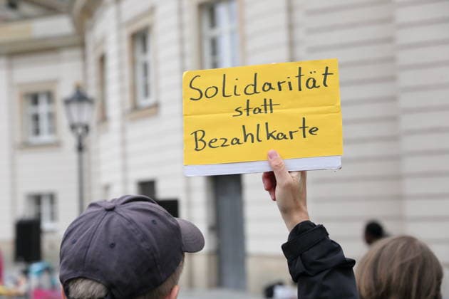A protester stands outside the state parliament holding a sign that reads Solidarity Instead of a Payment Card during a demonstration against the payment card for refugees in Brandenburg, Potsdam, September 25, 2026. Demonstration against the payment card in Potsdam