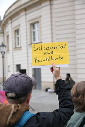 A protester stands outside the state parliament holding a sign that reads Solidarity Instead of a Payment Card during a demonstration against the payment card for refugees in Brandenburg, Potsdam, September 25, 2026. Demonstration against the payment card in Potsdam