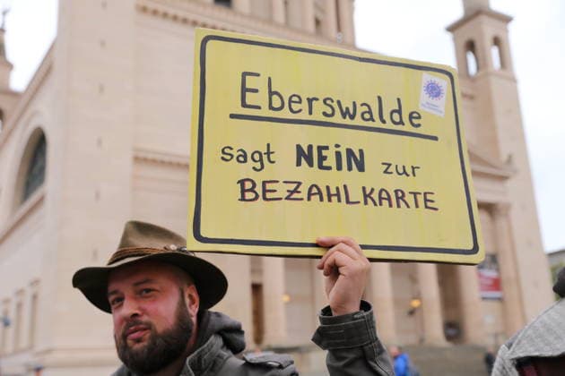 A protester stands outside the state parliament holding a sign that reads Eberswalde Says No to the Payment Card during a demonstration against the payment card for refugees in Brandenburg, Potsdam, September 25, 2026. Demonstration against the payment card in Potsdam