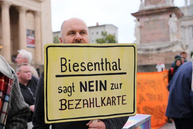 A protester stands outside the state parliament holding a sign that reads Biesenthal Says No to the Payment Card during a demonstration against the payment card for refugees in Brandenburg, Potsdam, September 25, 2026. Protest against the payment card in Potsdam
