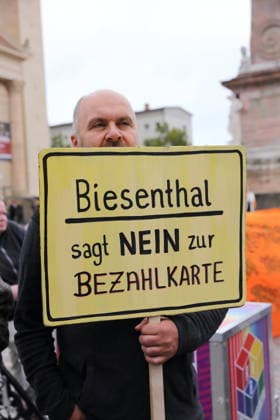 A protester stands outside the state parliament holding a sign that reads Biesenthal Says No to the Payment Card during a demonstration against the payment card for refugees in Brandenburg, Potsdam, September 25, 2026. Protest against the payment card in Potsdam