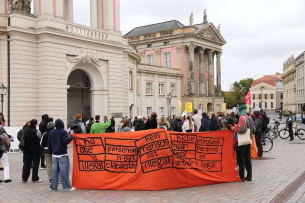 Protesters stand outside the state parliament holding banners reading No one is illegal, Personne n’est clandestine, Kein Mensch ist illegal, Hiçbir insan illegal degildir, and Ninguna persona es ilegal during a demonstration against the prepaid card for refugees in Brandenburg, Potsdam, September 25, 2026. Protest against the prepaid card in Potsdam