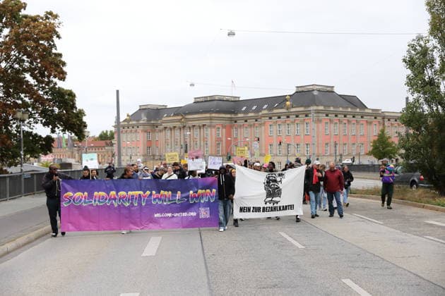 Protesters march across the Lange Brücke carrying banners reading Solidarity Will Win, Welcome United, and No to the Payment Card during a demonstration against the payment card for refugees in Brandenburg, Potsdam, September 25, 2026. Demonstration against the payment card in Potsdam