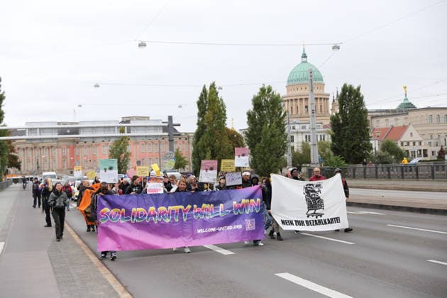 Protesters march across the Lange Brücke carrying banners reading Solidarity Will Win, Welcome United, and No to the Payment Card during a demonstration against the payment card for refugees in Brandenburg, Potsdam, September 25, 2026. Demonstration against the payment card in Potsdam