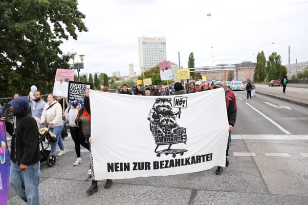 Protesters walk across the Lange Bridge carrying a banner reading No to the Payment Card during a demonstration against the payment card for refugees in Brandenburg, Potsdam, September 25, 2026. Protest against the payment card in Potsdam