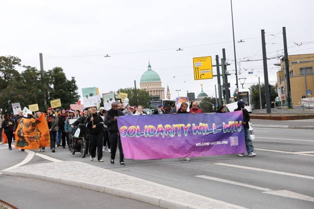 Protesters march down Heinrich Mann Allee carrying a banner reading Solidarity Will Win, Welcome United during a demonstration against the payment card for refugees in Brandenburg, Potsdam, September 25, 2026. Protest against the payment card in Potsdam