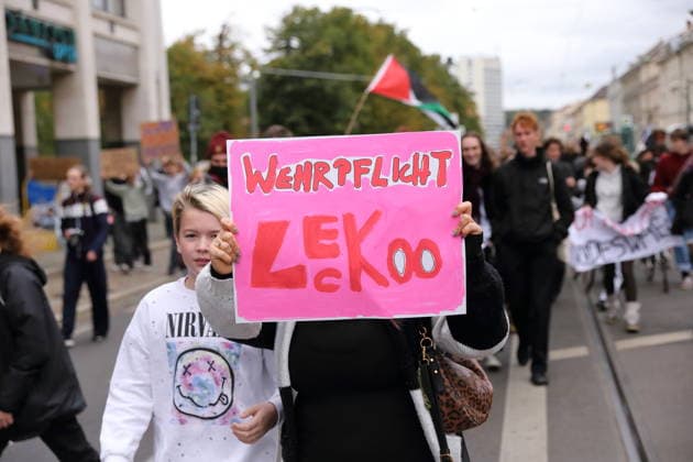A protester walks down Friedrich-Ebert-Straße holding a sign that reads Conscription: Screw That during a demonstration against conscription, Potsdam, September 25, 2026. School strike against conscription in Potsdam
