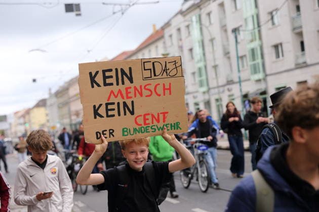 A protester walks down Friedrich-Ebert-Straße carrying a sign that reads No People, No Money for the Bundeswehr during a demonstration against the draft, Potsdam, September 25, 2026. School strike against the draft in Potsdam