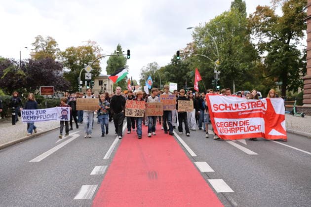 Protesters march with a banner reading No to Conscription, holding signs that say No to the Draft Center, The Rich Want War, Youth Want a Future, Don’t promote dying, School won’t help you on the front lines, and Boost social services, cut military spending, as well as a banner reading Sch