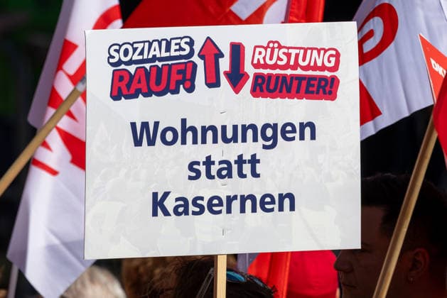 DGB Bavaria: Hard-Earned Large Rally, Nuremberg, September 26, 2026 A protest sign reading More for Social Programs, Less for Military Spending—Homes Instead of Barracks is held aloft at a rally. Red flags belonging to unions and participants can be seen in the background. Nuremberg, Bavaria, Germany 20260926-1V9A9728-M4000