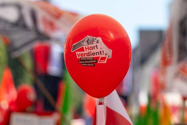 DGB Bavaria Hard-Earned Mass Rally, Nuremberg, September 26, 2026 A red balloon bearing the slogan Hard-Earned: Your Work, Your Health, Your Pension and the DGB logo towers over a crowd. In the blurred background, numerous red flags from a union rally can be seen. Nuremberg, Bavaria, Germany 20260926-1V9A9831-M4000