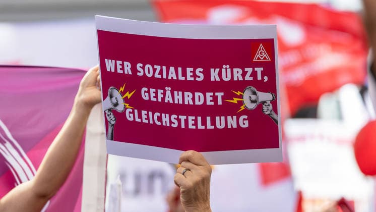 DGB Bavaria Hard Earned, Big Reward Rally, Nuremberg, September 26, 2026 A demonstrator holds an IG Metall sign reading Whoever cuts social programs jeopardizes equality. In the background, more red flags and banners from the rally can be seen. Nuremberg, Bavaria, Germany 20260926-1V9A9841-M4000