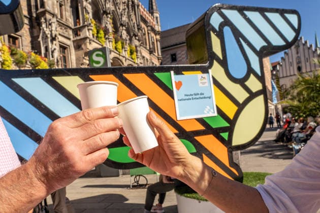 Münchner Olympia-Bewerbung erfolgreich, München wird deutscher Olympia-Bewerber, Münchner stoßen darauf an und auf einen Geburtstag, Olympia-Maskottchen Dackel Waldi auf dem Marienplatz, München, 26. September 2026 Deutschland, München, 26. September 2026, Münchner Olympia-Bewerbung erfolgreich, München wird deutscher Olympia-Bewerber, Mitglieder einer kleinen Geburtstagsparty stoßen auf Geburtstag und die Olympia-Entscheidung an, Sekt aus Pappbechern, Olympia-Maskottchen Dackel Waldi auf dem Marienplatz, Münchner Olympia-Bewerbung mit drei Meter hohem Riesen-Dackel, Schild: Heute fällt die Entscheidung, Marienplatz, Entscheidung des Deutschen Olympischen Sportbunds DOSB für München als Austragungsort der Olympiade 2036, 2040 o