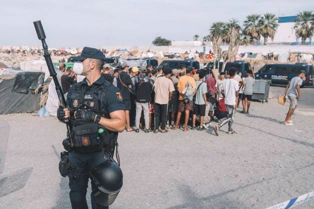 September 26, 2026, Ceuta, Ceuta, Spain: A Spanish National Police officer in riot gear holds a launcher as migrants gather behind him on the seafront of Ceuta. Thousands of migrants, most of them young Moroccan men, have been living in makeshift settlements in the Spanish North African enclave of Ceuta since a mass arrival at the end of July 2026 set off a migration and political crisis. Ceuta Spain  - ZUMAs392 20260926_zip_s392_005 Copyright: xFabianxSuspensivox