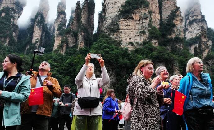 ZHANGJIAJIE, CHINA - OCTOBER 01: Tourists gather to celebrate the 77th anniversary of the founding of the People s Republic of China with activities including welcome drums, blocking-door wine, hand-waving dances, cake tasting and folk singing at the Bailong Elevator viewing platform in Zhangjiajie National Forest Park on October 1, 2026 in Zhangjiajie, Hunan Province of China. The scenic area organized various events to attract domestic and international visitors during the National Day holiday. Copyright: xVCGx 111670911305