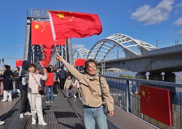 HARBIN, CHINA - OCTOBER 01: Residents wave national flags while red flags hang from the Binzhou Bridge on October 1, 2026 in Harbin, Heilongjiang Province of China. The city has decorated streets with flags and floral displays to celebrate the National Day holiday.  Copyright: xVCGx 111670933222