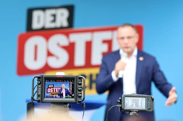 Enjoying a Bratwurst with Haseloff and Chrupalla, October 1, 2026, Doellstaedt, AfD event at Kiesling Roofing; enjoying a bratwurst with state parliament member Daniel Haseloff (AfD) and AfD national spokesperson Tino Chrupalla. Pictured: Tino Chrupalla giving a speech on stage, with the phrase The East is doing it in the background.