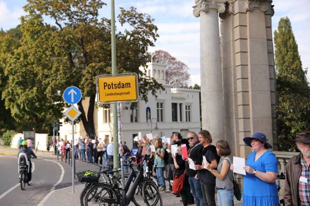 Protesters during a human chain for climate protection and democracy on the Glienicker Bridge in Potsdam, October 3, 2026. It s on fire —human chain in Potsdam