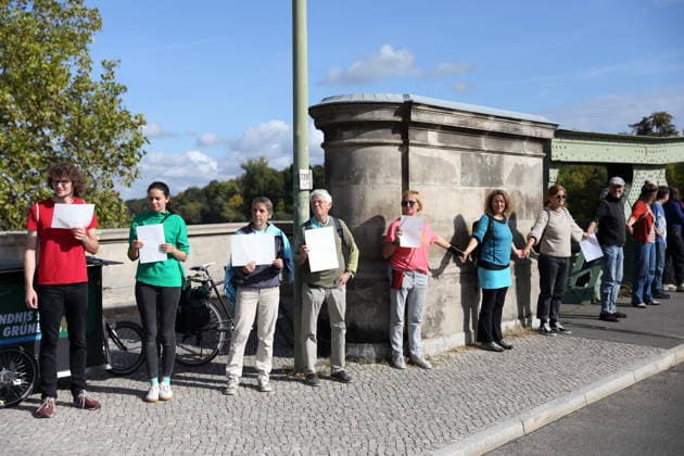Protesters during a human chain for climate protection and democracy on the Glienicker Bridge in Potsdam, October 3, 2026. It s on fire —human chain in Potsdam
