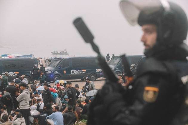 October 4, 2026, Ceuta, Ceuta, Spain: A riot police officer holds a launcher in front of migrants sitting on the ground during the eviction of the makeshift camp on El Trampolin beach in Ceuta. Spanish National Police began evicting the makeshift camp on El Trampolin beach in Ceuta on October 4, where more than 3,000 migrants, most of them young Moroccan men, were living. Dozens of police vans, armoured vehicles of the Police Intervention Units (UIP), drones and boats took part in the operation. People were taken by bus to the temporary centre at the Tarajal border to be identified, and the authorities plan to clear the beach in phases before October 15. The camp grew after a mass arrival at the end of July 2026 set off a migration and poli - ZUMAs392 20261004_zip_s392_015 Copyright: xFabianxSuspensivox