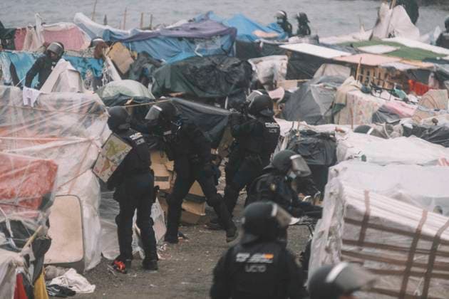 October 4, 2026, Ceuta, Ceuta, Spain: Riot police officers pull down the plastic sheeting of a shelter during the eviction of the makeshift migrant camp on El Trampolin beach in Ceuta. Spanish National Police began evicting the makeshift camp on El Trampolin beach in Ceuta on October 4, where more than 3,000 migrants, most of them young Moroccan men, were living. Dozens of police vans, armoured vehicles of the Police Intervention Units (UIP), drones and boats took part in the operation. People were taken by bus to the temporary centre at the Tarajal border to be identified, and the authorities plan to clear the beach in phases before October 15. The camp grew after a mass arrival at the end of July 2026 set off a migration and political cri  - ZUMAs392 20261004_zip_s392_018 Copyright: xFabianxSuspensivox