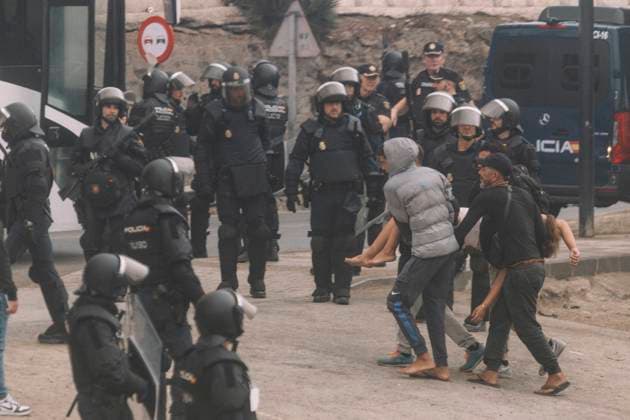 October 4, 2026, Ceuta, Ceuta, Spain: A young man runs past a line of riot police officers next to a bus during the eviction of the makeshift migrant camp on El Trampolin beach in Ceuta. Spanish National Police began evicting the makeshift camp on El Trampolin beach in Ceuta on October 4, where more than 3,000 migrants, most of them young Moroccan men, were living. Dozens of police vans, armoured vehicles of the Police Intervention Units (UIP), drones and boats took part in the operation. People were taken by bus to the temporary centre at the Tarajal border to be identified, and the authorities plan to clear the beach in phases before October 15. The camp grew after a mass arrival at the end of July 2026 set off a migration and political c - ZUMAs392 20261004_zip_s392_010 Copyright: xFabianxSuspensivox