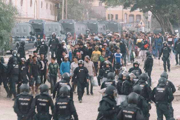 October 4, 2026, Ceuta, Ceuta, Spain: Dozens of young migrants walk escorted by riot police officers during the eviction of the makeshift camp on El Trampolin beach in Ceuta. Spanish National Police began evicting the makeshift camp on El Trampolin beach in Ceuta on October 4, where more than 3,000 migrants, most of them young Moroccan men, were living. Dozens of police vans, armoured vehicles of the Police Intervention Units (UIP), drones and boats took part in the operation. People were taken by bus to the temporary centre at the Tarajal border to be identified, and the authorities plan to clear the beach in phases before October 15. The camp grew after a mass arrival at the end of July 2026 set off a migration and political crisis. Ceut - ZUMAs392 20261004_zip_s392_044 Copyright: xFabianxSuspensivox