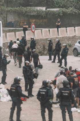 October 4, 2026, Ceuta, Ceuta, Spain: Riot police officers stand among migrants and their bags during the eviction of the makeshift camp on El Trampolin beach in Ceuta. Spanish National Police began evicting the makeshift camp on El Trampolin beach in Ceuta on October 4, where more than 3,000 migrants, most of them young Moroccan men, were living. Dozens of police vans, armoured vehicles of the Police Intervention Units (UIP), drones and boats took part in the operation. People were taken by bus to the temporary centre at the Tarajal border to be identified, and the authorities plan to clear the beach in phases before October 15. The camp grew after a mass arrival at the end of July 2026 set off a migration and political crisis. Ceuta Spai - ZUMAs392 20261004_zip_s392_032 Copyright: xFabianxSuspensivox