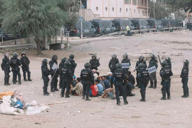 October 4, 2026, Ceuta, Ceuta, Spain: Riot police officers surround a group of migrants sitting on the ground, with a line of police vans behind, during the eviction of the makeshift camp on El Trampolin beach in Ceuta. Spanish National Police began evicting the makeshift camp on El Trampolin beach in Ceuta on October 4, where more than 3,000 migrants, most of them young Moroccan men, were living. Dozens of police vans, armoured vehicles of the Police Intervention Units (UIP), drones and boats took part in the operation. People were taken by bus to the temporary centre at the Tarajal border to be identified, and the authorities plan to clear the beach in phases before October 15. The camp grew after a mass arrival at the end of July 2026 se - ZUMAs392 20261004_zip_s392_043 Copyright: xFabianxSuspensivox