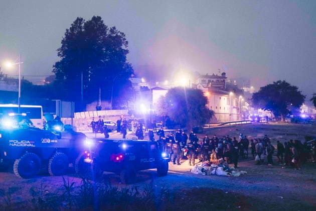 October 4, 2026, Ceuta, Ceuta, Spain: Police vans and an armoured vehicle with flashing blue lights at night during the eviction of the makeshift migrant camp on El Trampolin beach in Ceuta. Spanish National Police began evicting the makeshift camp on El Trampolin beach in Ceuta on October 4, where more than 3,000 migrants, most of them young Moroccan men, were living. Dozens of police vans, armoured vehicles of the Police Intervention Units (UIP), drones and boats took part in the operation. People were taken by bus to the temporary centre at the Tarajal border to be identified, and the authorities plan to clear the beach in phases before October 15. The camp grew after a mass arrival at the end of July 2026 set off a migration and politic - ZUMAMigr 20261004_zip_s392_039 Copyright: xFabianxSuspensivox