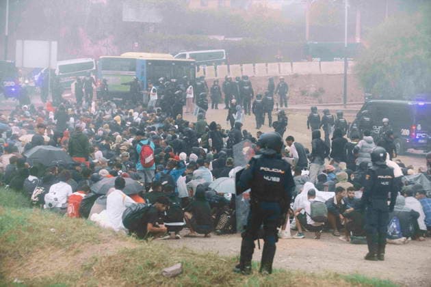 October 4, 2026, Ceuta, Ceuta, Spain: Migrants sit on the ground guarded by riot police, with buses waiting behind, during the eviction of the makeshift camp on El Trampolin beach in Ceuta. Spanish National Police began evicting the makeshift camp on El Trampolin beach in Ceuta on October 4, where more than 3,000 migrants, most of them young Moroccan men, were living. Dozens of police vans, armoured vehicles of the Police Intervention Units (UIP), drones and boats took part in the operation. People were taken by bus to the temporary centre at the Tarajal border to be identified, and the authorities plan to clear the beach in phases before October 15. The camp grew after a mass arrival at the end of July 2026 set off a migration and politica - ZUMAMigr 20261004_zip_s392_014 Copyright: xFabianxSuspensivox