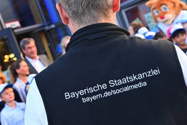 The back of a person with the words Bavarian State Chancellery, Social media takes center stage at a school visit with Minister President Markus Söder Markus SÖDER, Minister President of Bavaria and CSU