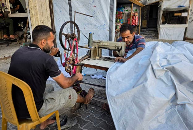 Palestinian Tailor Repairs Tent Covers for Displaced Families in Khan Younis Palestinian tailor Shaaban al-Tabash repairs and assembles tarpaulins and plastic sheets using rudimentary methods to reinforce the tents of displaced Palestinians and protect them from cold weather and rain in Khan Younis, in the southern Gaza Strip, on October 4, 2026. As winter approaches, shortages of protective supplies and the deterioration of many tents after nearly three years of war are worsening living conditions, while al-Tabash uses available materials to extend the life of shelters that have become the last refuge for thousands of displaced people. Photo by Tariq Mohammad APA Images Khan Yunis Gaza Strip Palestinian Territory 041026_Khan_Yunis_TM_01( Copyright: xapaimagesxTariqxMohammad xapaimagesx