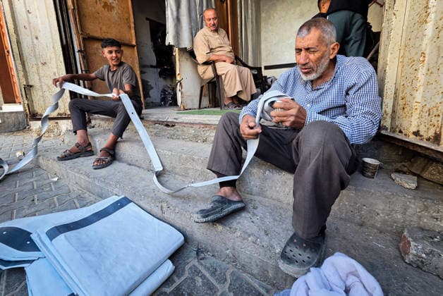 Palestinian Tailor Repairs Tent Covers for Displaced Families in Khan Younis Palestinian tailor Shaaban al-Tabash repairs and assembles tarpaulins and plastic sheets using rudimentary methods to reinforce the tents of displaced Palestinians and protect them from cold weather and rain in Khan Younis, in the southern Gaza Strip, on October 4, 2026. As winter approaches, shortages of protective supplies and the deterioration of many tents after nearly three years of war are worsening living conditions, while al-Tabash uses available materials to extend the life of shelters that have become the last refuge for thousands of displaced people. Photo by Tariq Mohammad APA Images Khan Yunis Gaza Strip Palestinian Territory 041026_Khan_Yunis_TM_01( Copyright: xapaimagesxTariqxMohammad xapaimagesx