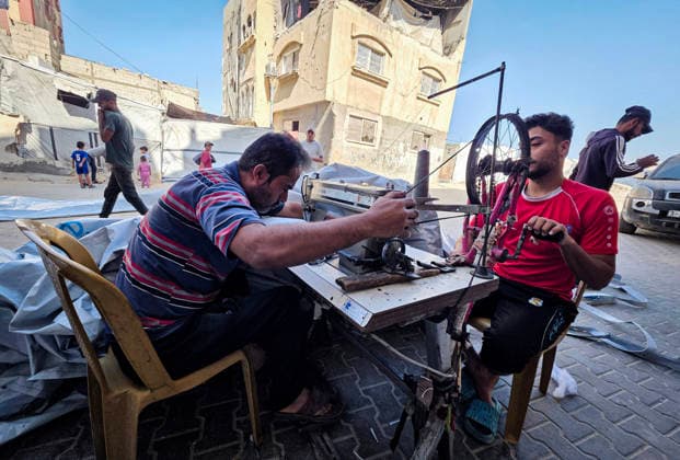 Palestinian Tailor Repairs Tent Covers for Displaced Families in Khan Younis Palestinian tailor Shaaban al-Tabash repairs and assembles tarpaulins and plastic sheets using rudimentary methods to reinforce the tents of displaced Palestinians and protect them from cold weather and rain in Khan Younis, in the southern Gaza Strip, on October 4, 2026. As winter approaches, shortages of protective supplies and the deterioration of many tents after nearly three years of war are worsening living conditions, while al-Tabash uses available materials to extend the life of shelters that have become the last refuge for thousands of displaced people. Photo by Tariq Mohammad APA Images Khan Yunis Gaza Strip Palestinian Territory 041026_Khan_Yunis_TM_01( Copyright: xapaimagesxTariqxMohammad xapaimagesx