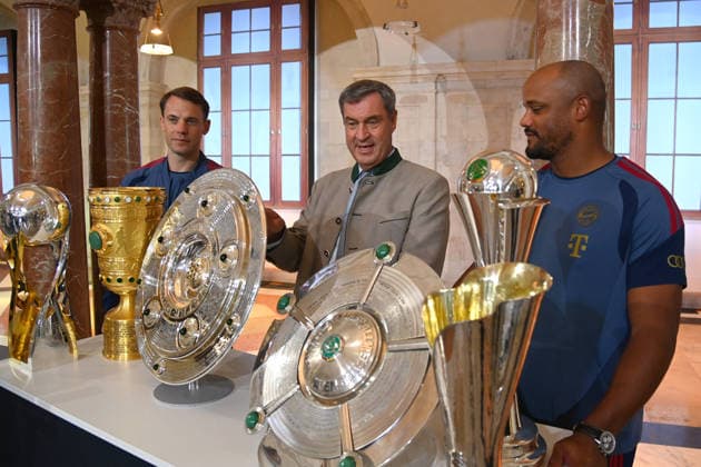 From left: Manuel NEUER, goalkeeper for Bayern Munich; Markus SOEDER, Minister-President of Bavaria and CSU Chairman; and Vincent KOMPANY, coach of Bayern Munich, stand behind the trophies, cups, and awards won during the 2025–26 season,Championship Trophy, DFB Cup, and Super Cup. Markus SÖDER, Minister-President of Bavaria and CSU Chairman, receives the championship teams of FC Bayern Munich in the Kuppelsaal at the State Chancellery in Munich on September 16, 2026.